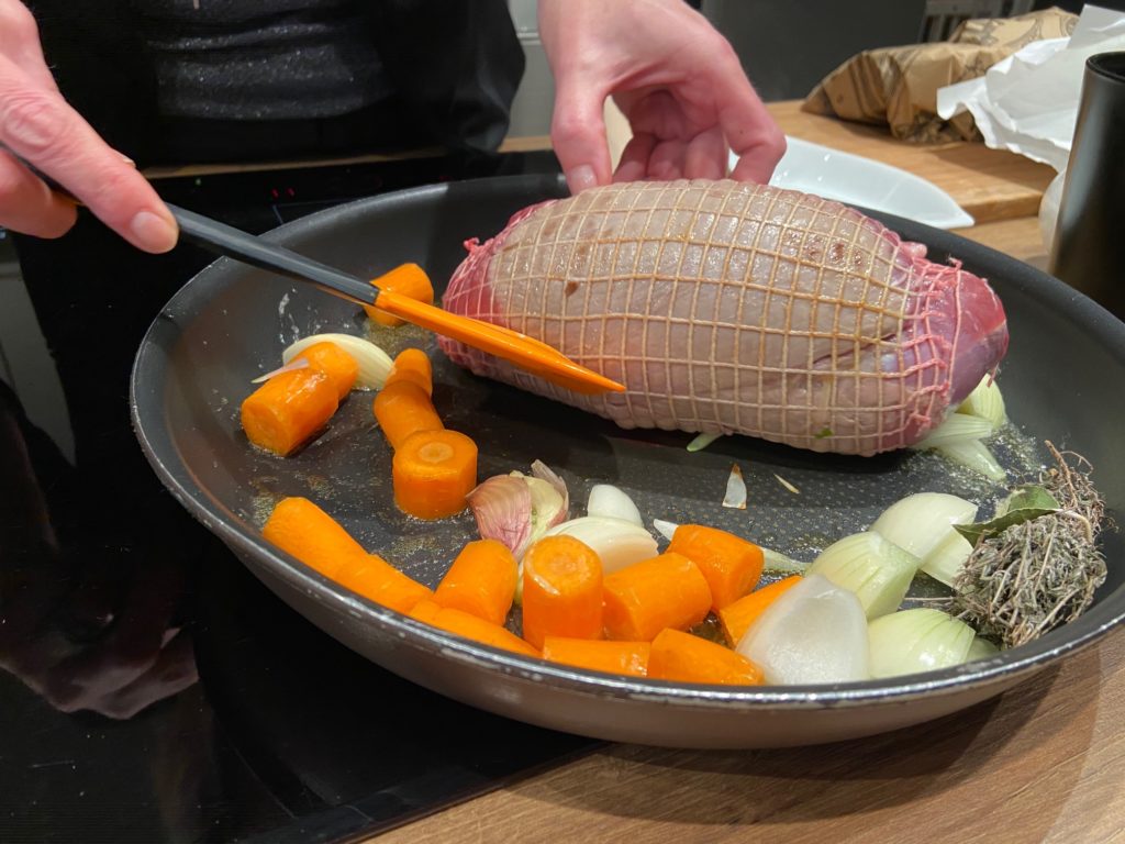 Le rôti de gigue de chevreuil est cuit à la poêle dans un premier temps avec les carottes, les oignons et le bouquet garni.